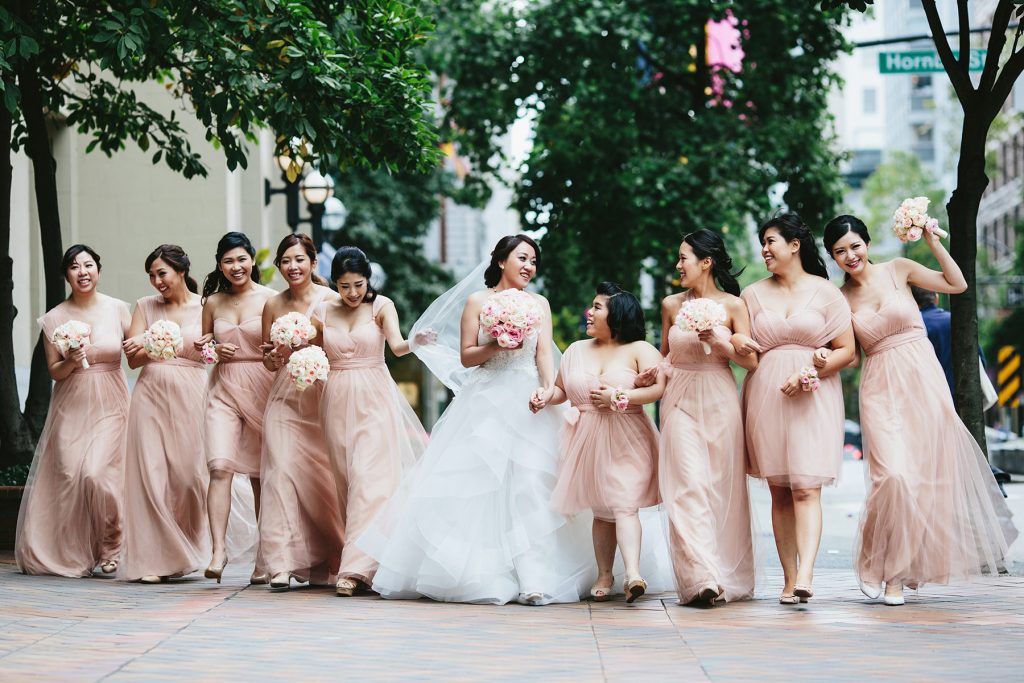 bridesmaids in blush pink dresses walk down west hastings street in front of the vancouver club www.lucida-photography.com
