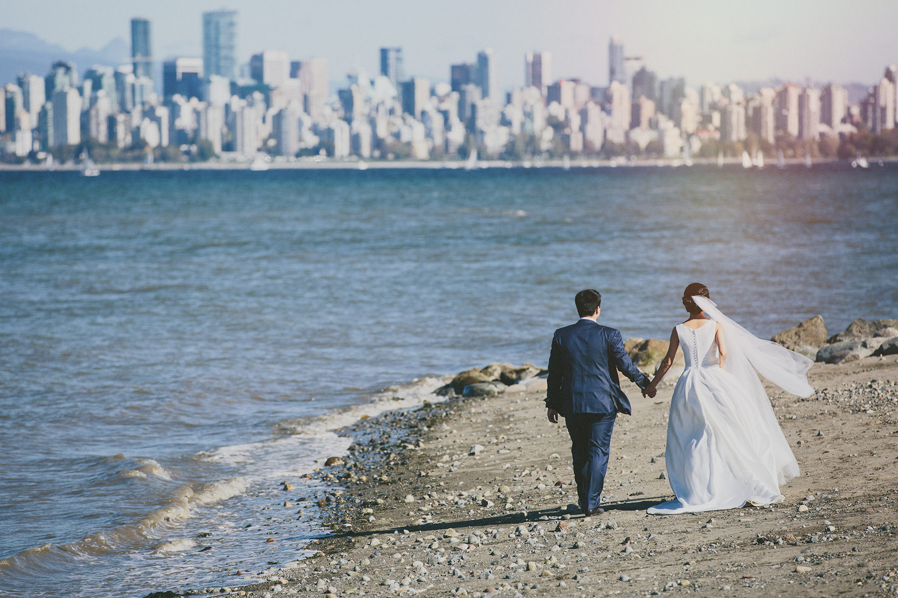 a bride and groom stroll Jericho beach with a view of downtown vancouver before them www.lucida-photography.com
